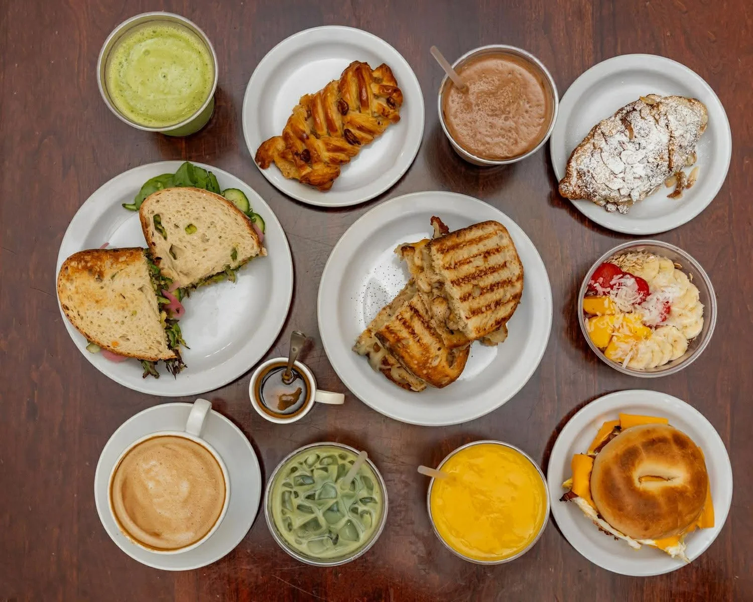 Overhead spread of Pluto sandwiches, paninis, pastries, smoothies, matcha, and coffee